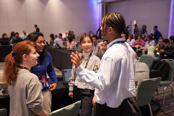 attendees talking at the front of a room of people at tables and people standing